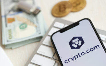 KYIV, UKRAINE - MARCH 15, 2024 Crypto com logo on iPhone display screen on white keyboard with money and bitcoins. Cryptocurrency exchange portal